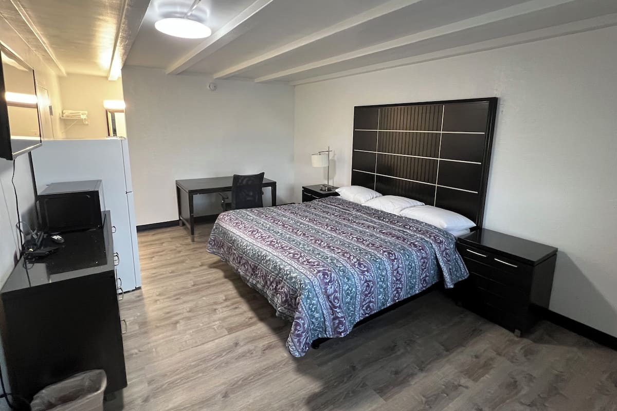 A hotel room with a bed, a desk, a chair, a TV, and a bedside table.