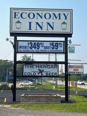 A sign for Economy Inn with pricing for weekly and daily rates, amenities like full-size fridges and microwaves, and a sign for The Hangar offering cold beer.