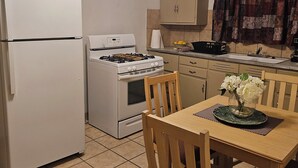 Eine kompakte Küche mit Kühlschrank, Herd und Backofen. Ein Esstisch mit Stühlen und eine Blumenvase sind ebenfalls vorhanden.