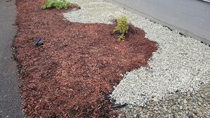 Ein Innenhof mit Kies- und Holzmulch-Boden, einem Holzzaun und einer grauen Wand.