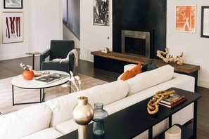 Un salon moderne avec un canapé, un fauteuil, une table basse, une cheminée et des œuvres d’art accrochées aux murs.