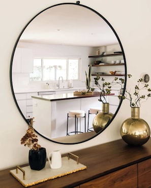 Een keuken met witte kasten, een centraal eiland, barstoelen en een grote spiegel aan de wand.