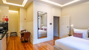 Habitación de hotel con piso de madera, una cama, un escritorio con silla, un espejo y un armario.