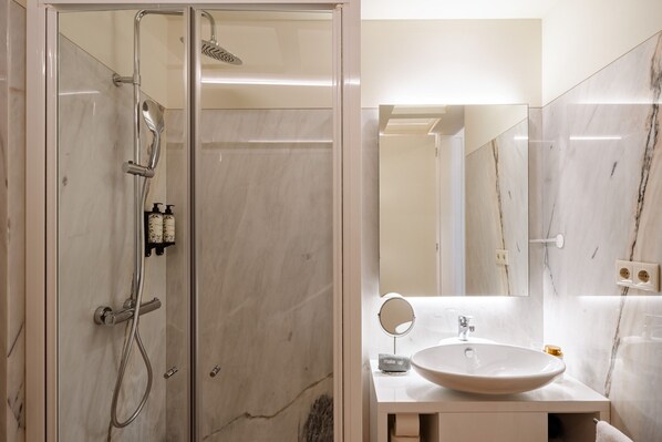 A bathroom with a glass-enclosed shower, a sink, a mirror, and marble walls.