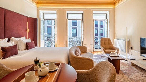 Quarto de hotel com uma cama grande, duas poltronas, uma mesinha com bandeja e uma televisão.