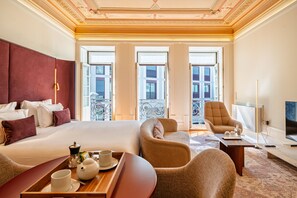A hotel room with a large bed, two armchairs, a small table with a tray, and a TV.
