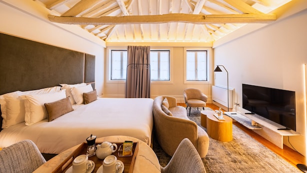 Una habitación de hotel con una cama grande, un sofá, un televisor y una bandeja con tazas y una tetera.