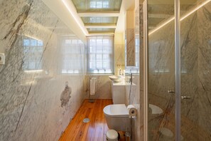 A modern bathroom with a wooden floor, marble walls, a glass shower enclosure, and a skylight. - Intimate Studio near Bolhao Market (Oporto)
