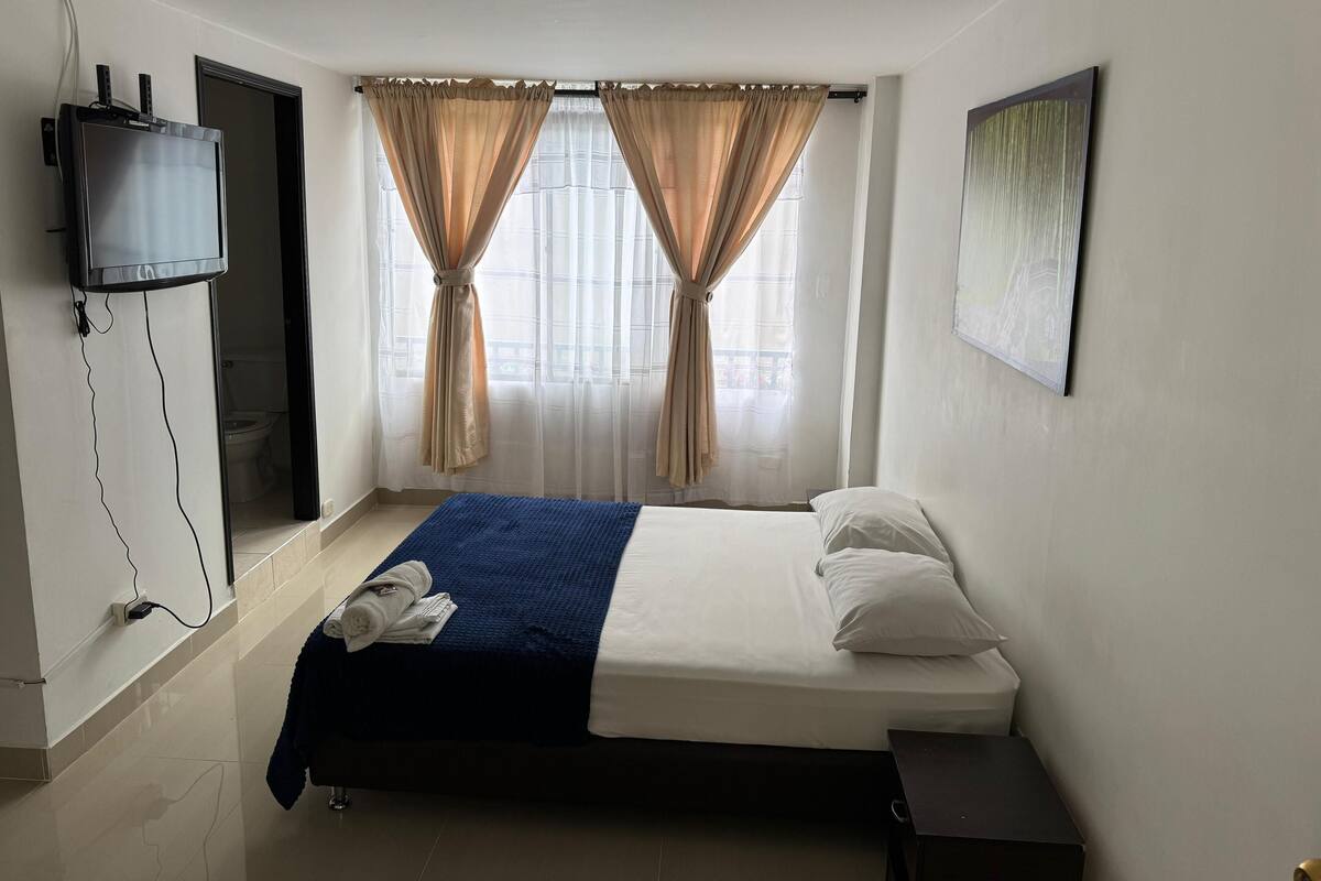 Een hotelkamer met een bed, een aan de muur bevestigde televisie en een raam met gordijnen.