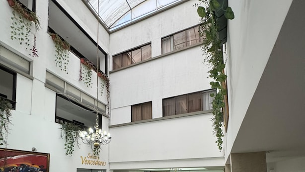 Een ruime, overdekte ruimte met een hoge plafond, diverse zithoeken en potplanten.