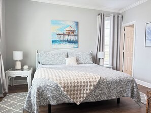 A bedroom with a bed, nightstands, a painting, and a view of the outdoors. - Babe’s Beach Gulf View + 2BR/2BA + Pools + Balcony (Galveston)
