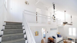 Amplia sala de estar con escalera, un sofá blanco y un ventilador de techo.
