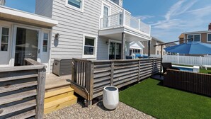 Una casa de dos pisos con balcón, una pequeña terraza y un patio trasero con césped artificial y piscina.