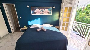 Een slaapkamer met een bed, kussens, een schilderij, een klein tafeltje en een balkon met een hekwerk.