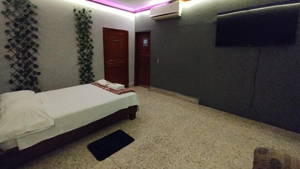 Een slaapkamer met een bed, een zwarte mat, een aan de muur bevestigde televisie en een deur met een bordje.