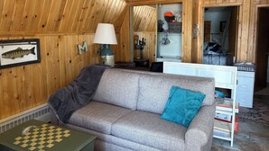Een kamer met een houten wand, een bank, een lamp, een afbeelding van een vis in een lijst, en een bureau met een mandje.