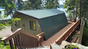 Een chalet met een metalen dak, een houten terras en een pad van stenen dat naar de ingang leidt.