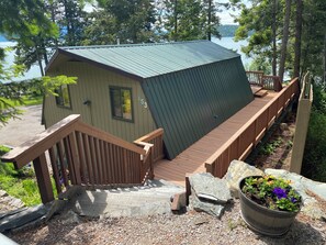 Een chalet met een metalen dak, een houten terras en een pad van stenen dat naar de ingang leidt.