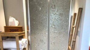 Ein Badezimmer mit einem hölzernen Ablagebrett, das Handtücher trägt, einer Milchglasschiebetür und einer Holzleiter, die an der Wand lehnt.