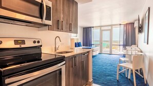 A modern kitchen with a microwave, stove, and sink. There is a dining area with a table and chairs, and a balcony with a view.