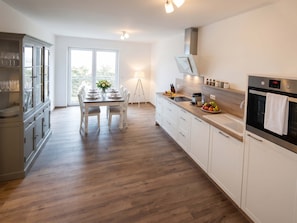 A modern kitchen with a dining area, wooden flooring, and a view through the window.