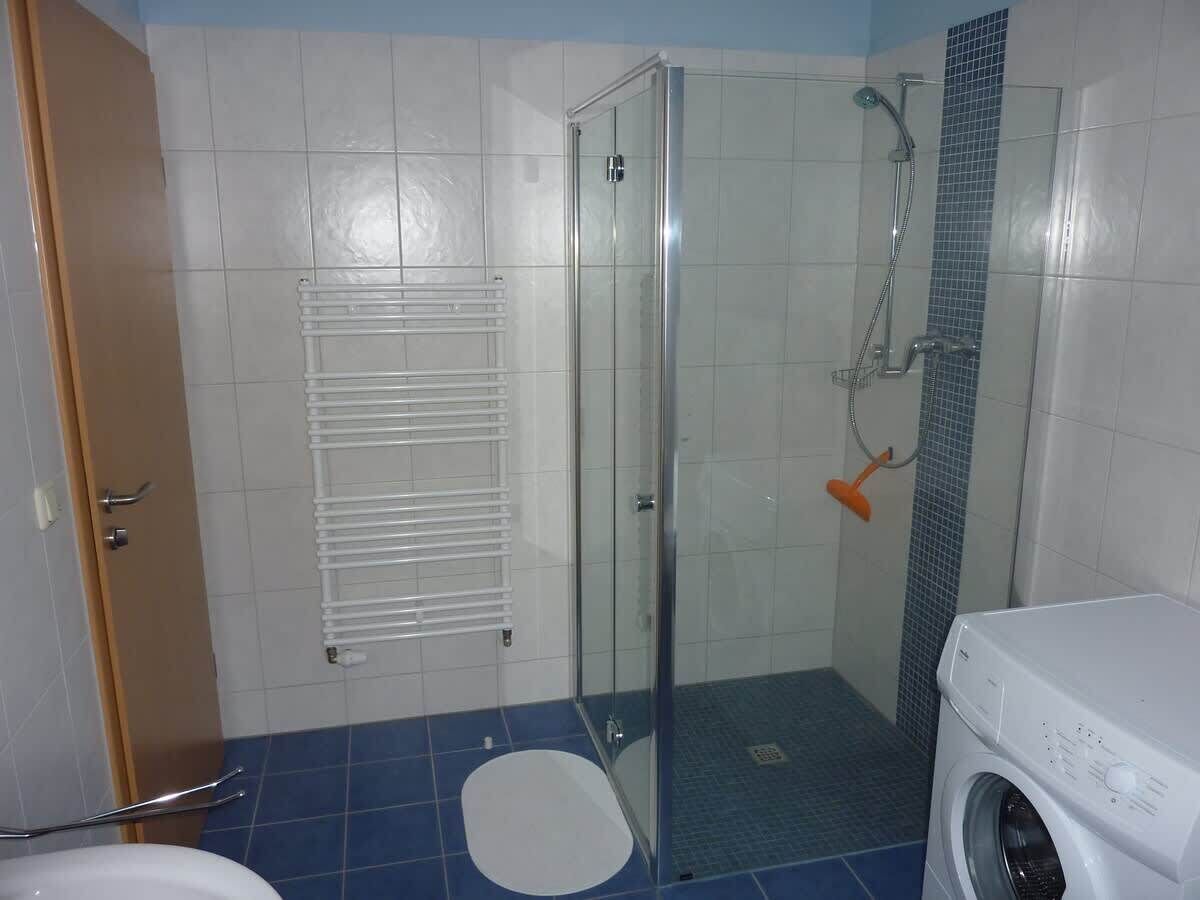 Ein Badezimmer mit Duschkabine, weißer Toilette, Waschmaschine und gefliestem Boden.