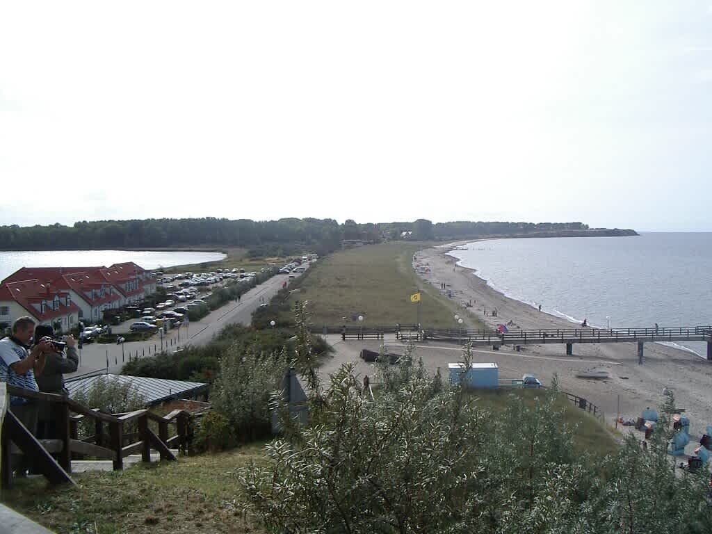 Une vue sur la côte, avec une plage, des voitures garées et quelques personnes.