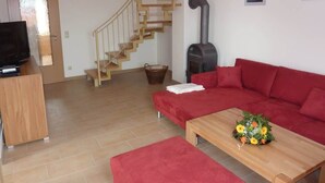 A living room with a red sofa, wooden coffee table, and a TV stand. A wooden staircase is visible in the background. - Ferienhaus Nemo Wohnung 6 "Dorie" (Rerik)