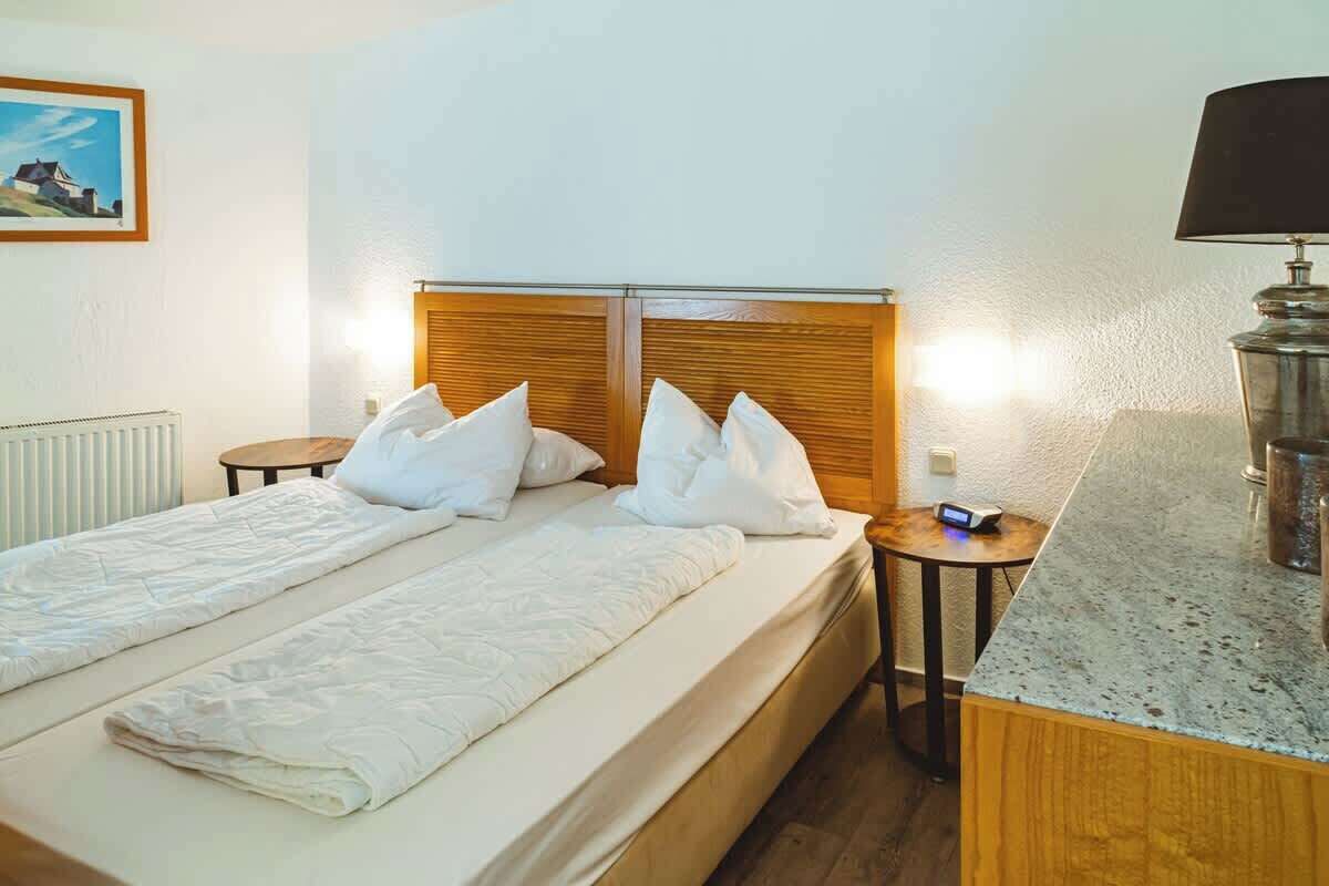 A hotel room with a double bed, a wooden headboard, a small bedside table with a lamp, and a view of the sea.