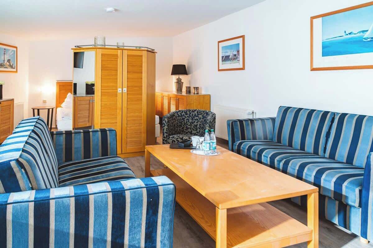 Une pièce avec des canapés à rayures, une table en bois, une armoire et un téléviseur posé sur un meuble.