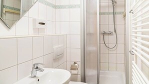 Ein Badezimmer mit weißem Waschbecken, einem Spiegel, einer Duschkabine und einem Handtuchhalter.