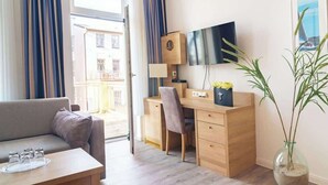 A modern room with a sofa, a wooden desk, a TV, and a large window with curtains. - Passat (Rostock)