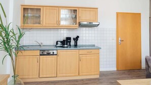 A compact kitchen with wooden cabinets, a built-in stove, and a coffee maker. - Passat (Rostock)