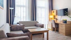 A modern hotel room with a sofa, a wooden desk, a television, and a large window with curtains. - Passat (Rostock)