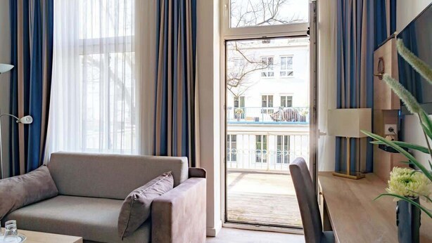 A modern living room with a sofa, a dining table, and a view of a building through a glass door. - Passat (Rostock)