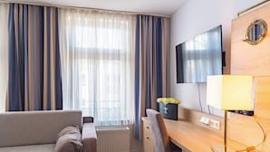 A hotel room with a sofa, a desk, a TV, and a lamp. - Sedov (Rostock)