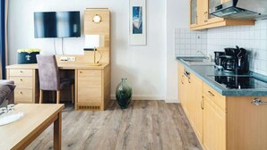 A compact hotel room with a wooden desk, a flat-screen TV, a small kitchenette, and a large window. - Sedov (Rostock)