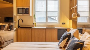 Une chambre compacte comprenant un lit, un four à micro-ondes encastré, un évier et une fenêtre avec des stores.