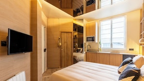 Une chambre compacte comprenant un lit, une télévision, une armoire et un coin cuisine.