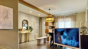 Un soggiorno moderno con una grande TV a schermo piatto, pavimento in legno e un’accogliente zona salotto con una panca e un tavolino da caffè.
