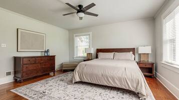 A bedroom with a bed, dresser, nightstands, a ceiling fan, and a window with blinds.