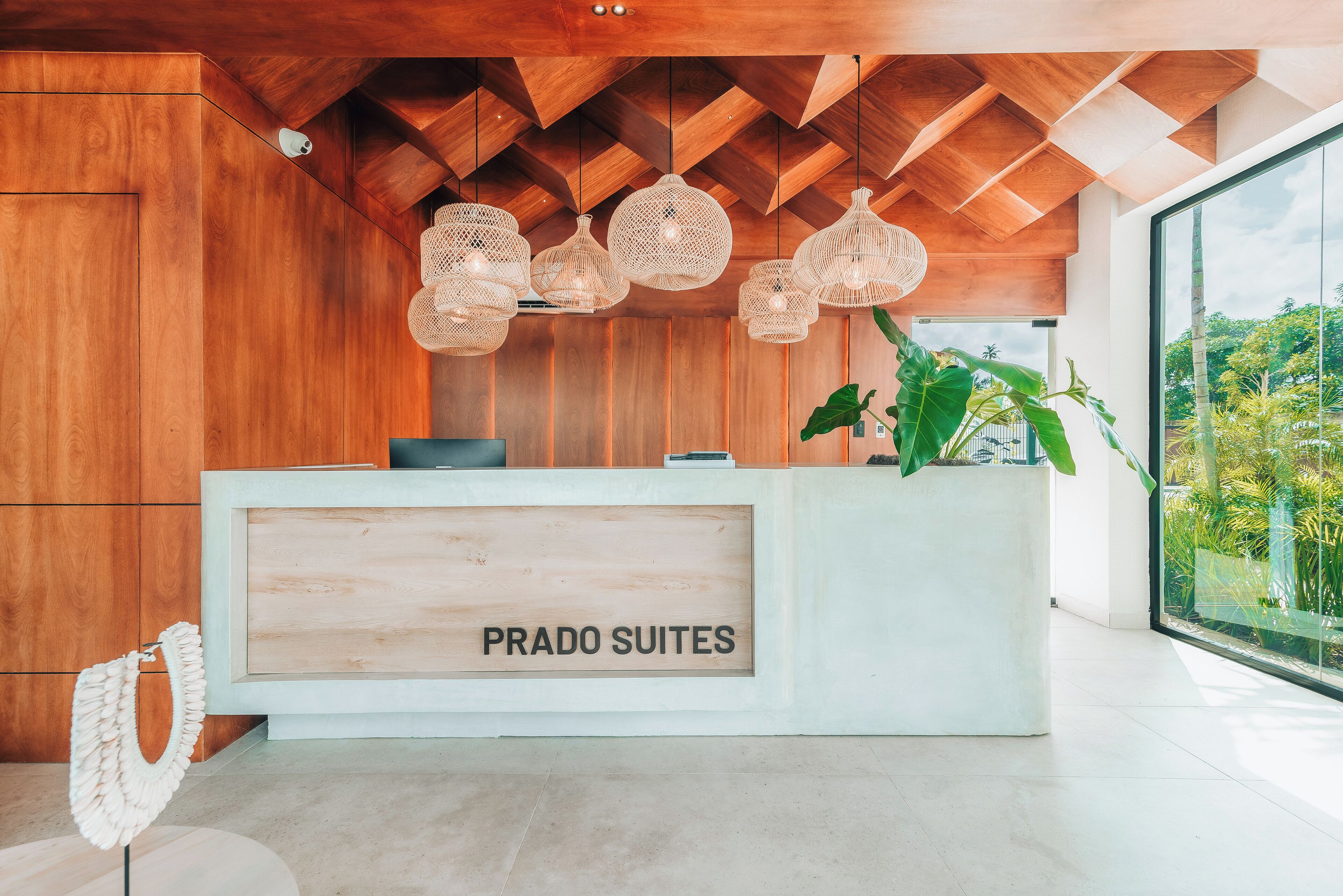 Un mostrador de recepción con un cartel que dice "PRADO SUITES" y un amplio ventanal con vistas a zonas verdes.