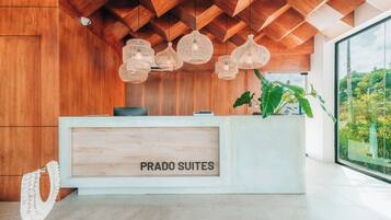 Un mostrador de recepción con un cartel que dice "PRADO SUITES" y un amplio ventanal con vistas a zonas verdes.