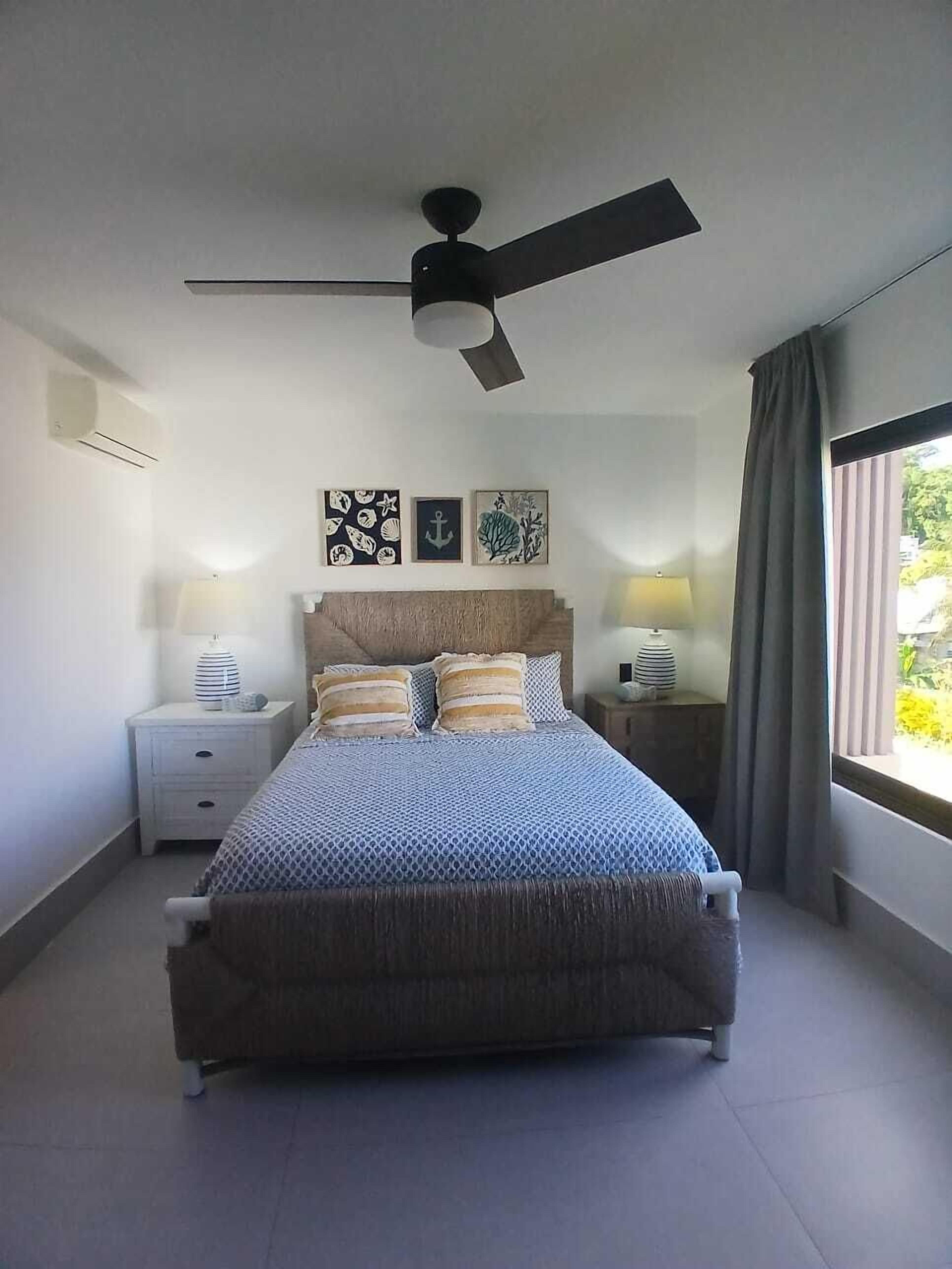 A bedroom with a bed, two bedside tables, a ceiling fan, and artwork on the wall.