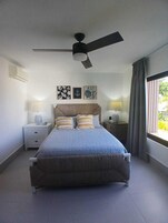 Un dormitorio con una cama, dos mesitas de noche, un ventilador de techo y una obra de arte en la pared.