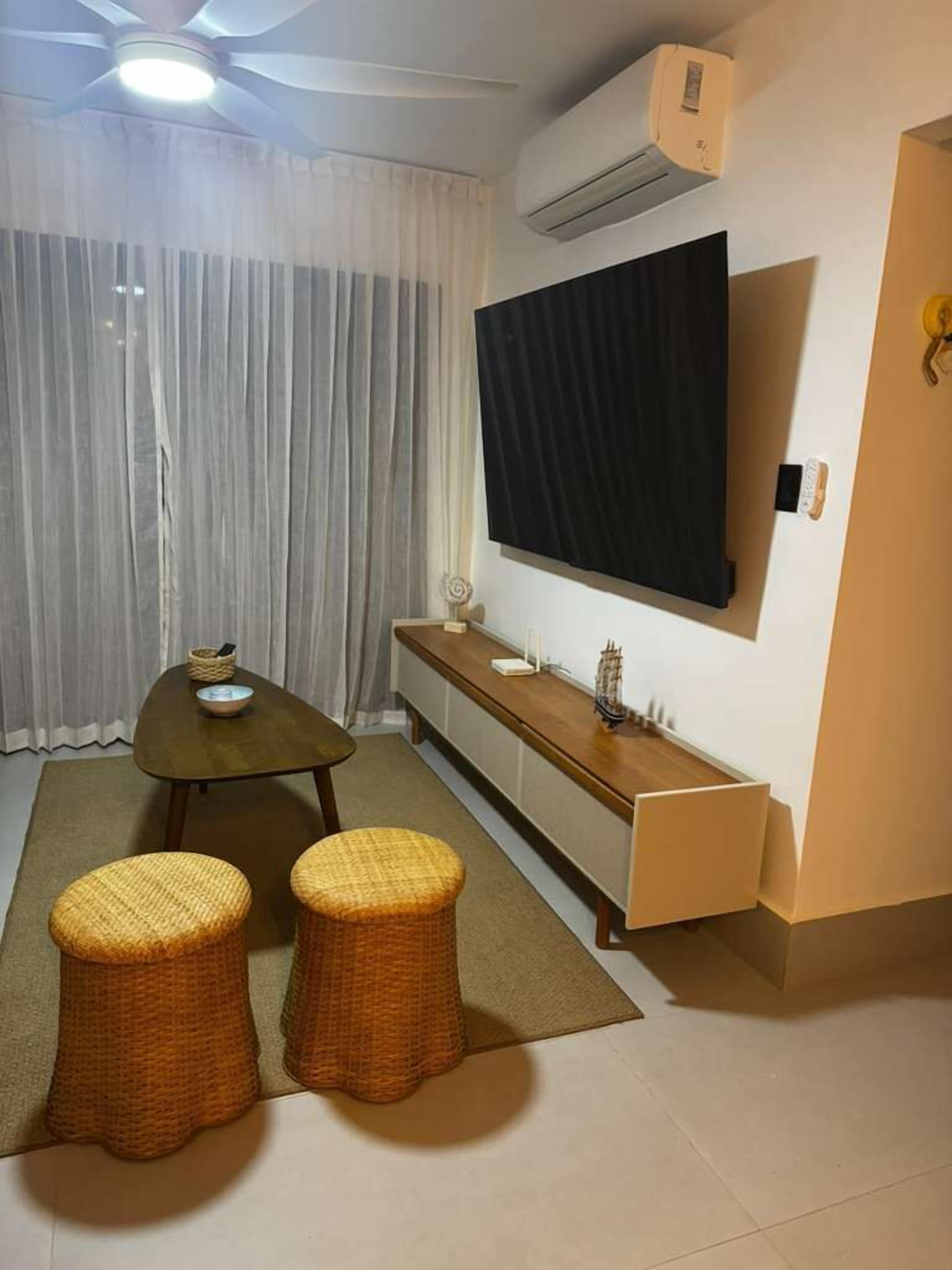 A modern room with a dining table, two wicker stools, a flat-screen TV mounted on the wall, and an air conditioning unit.