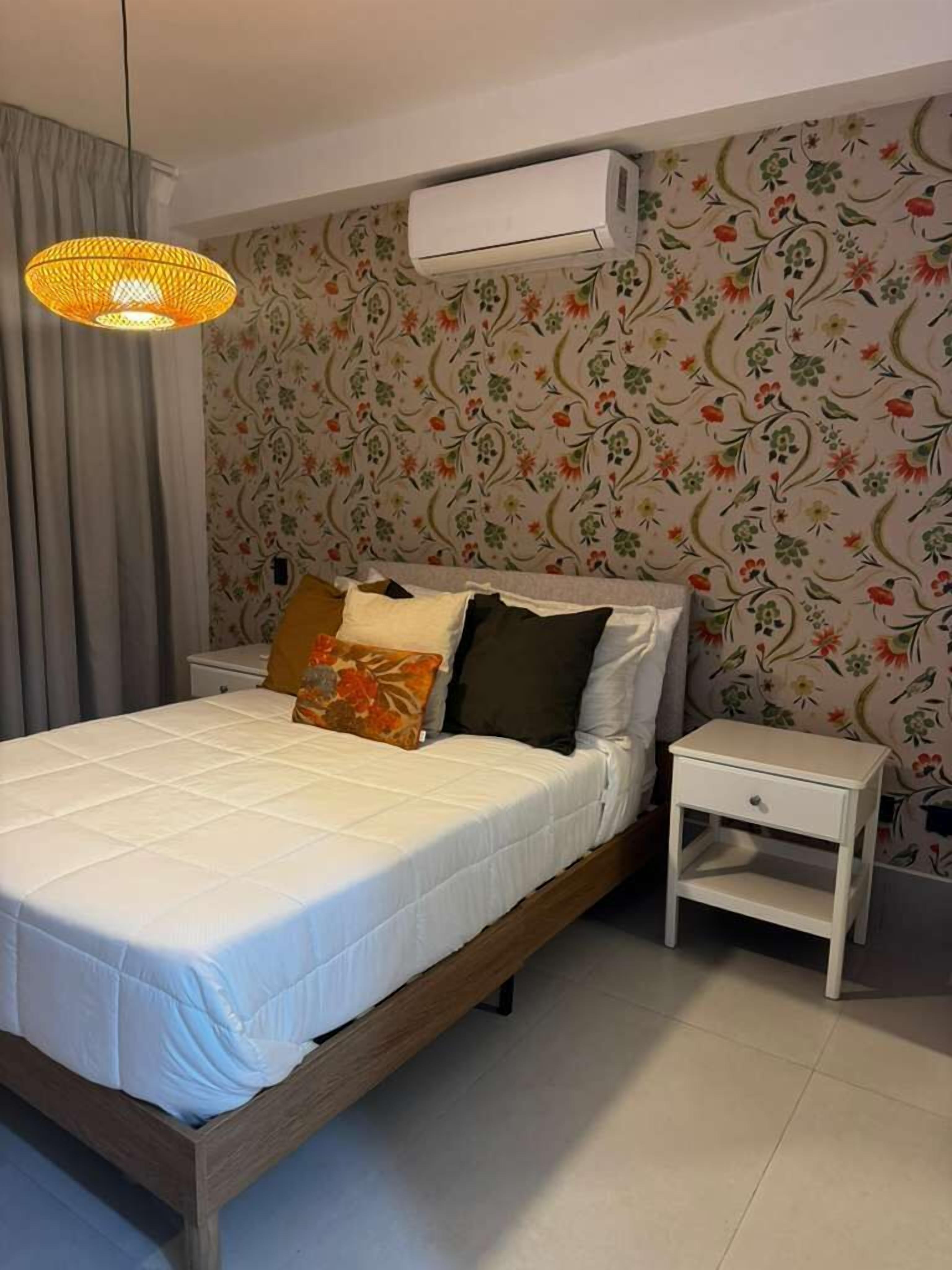 Ein Schlafzimmer mit einem Bett, einem Nachttisch, einer Hängelampe und einer Klimaanlage.