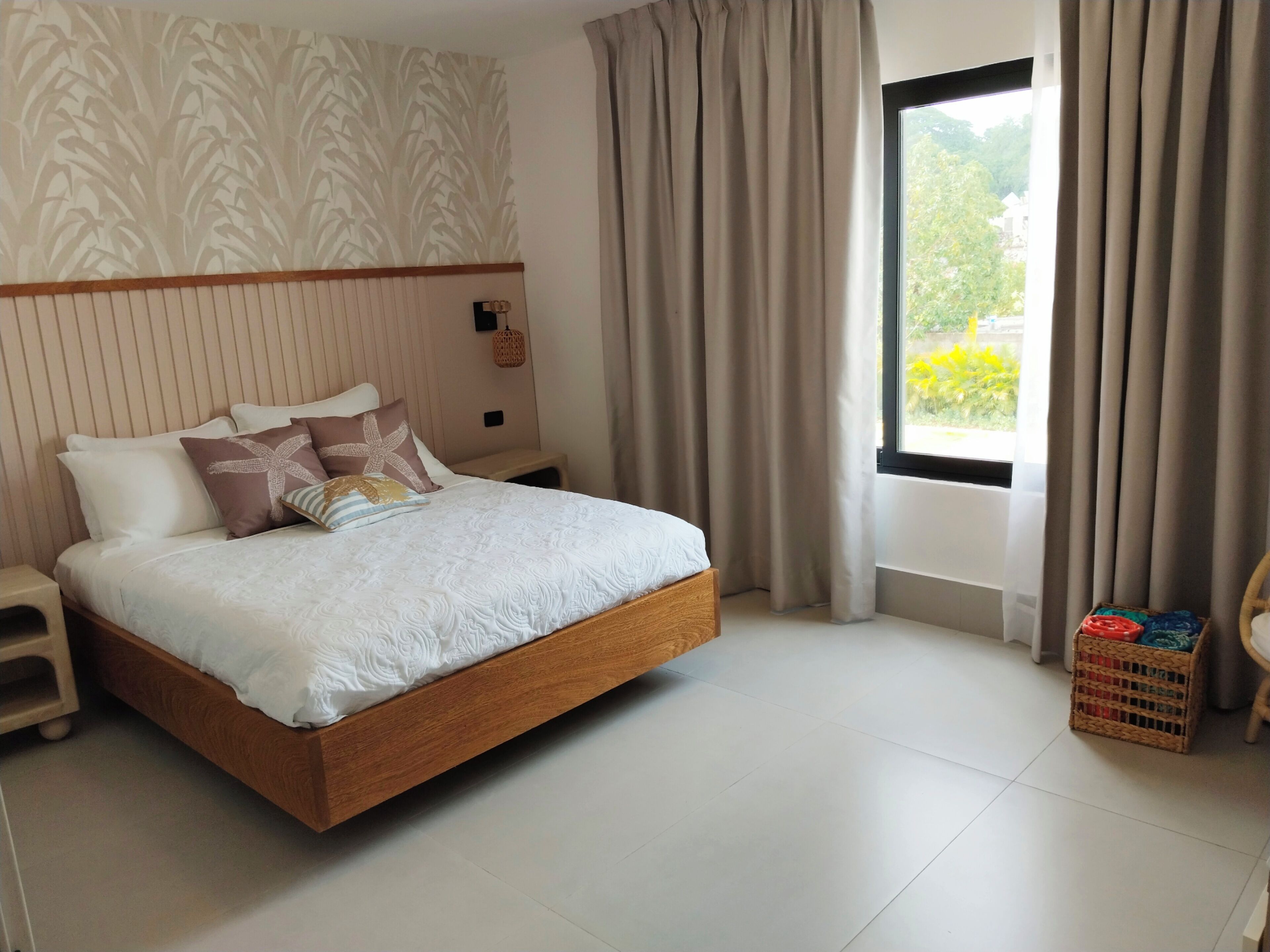 Een keurig opgemaakt slaapkamer met een houten bed, een nachtkastje, een klein tafeltje en een rieten mand.