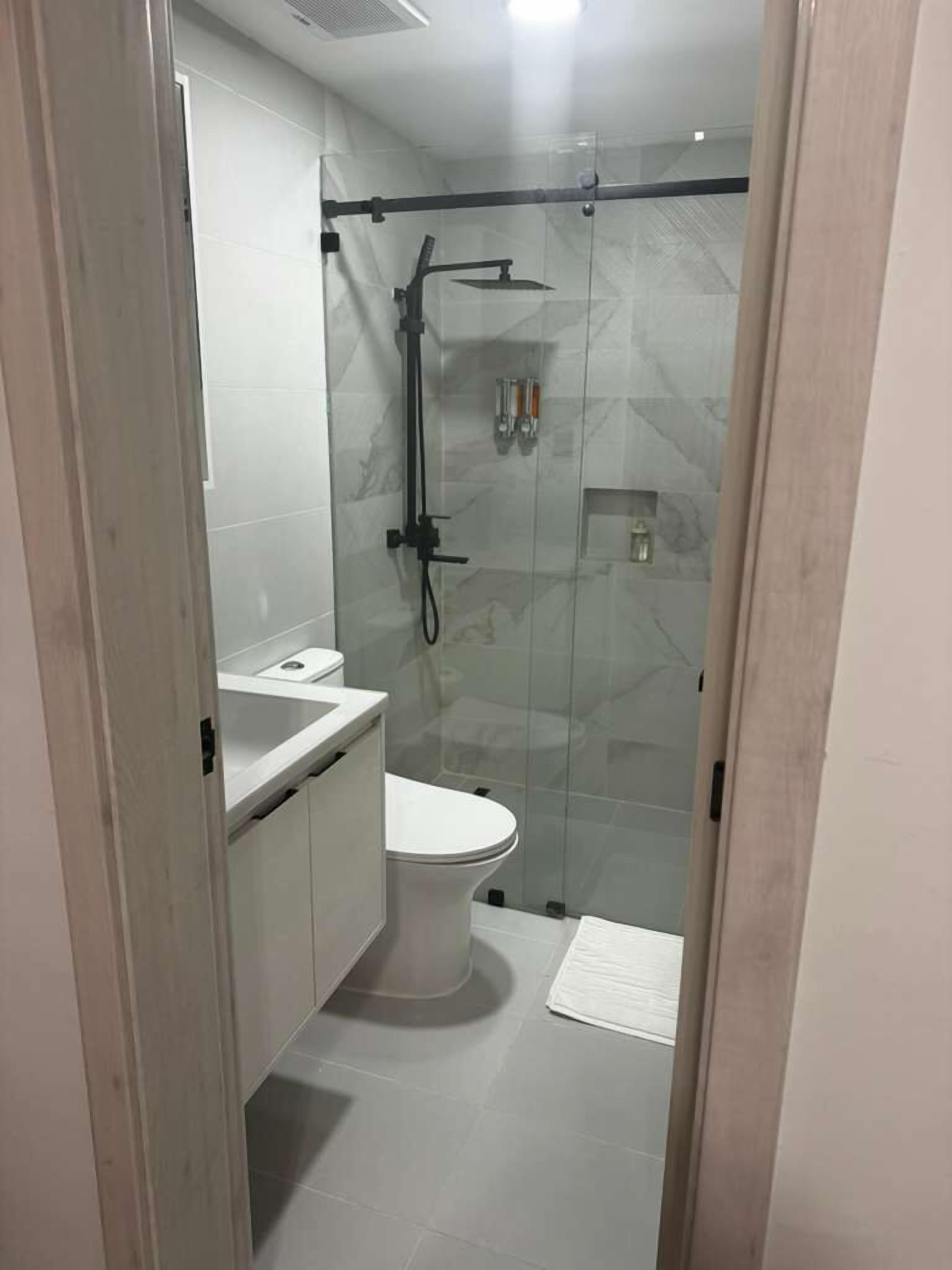 A modern bathroom with a glass-enclosed shower, a white toilet, and a sink with a mirror.