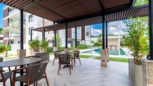 A covered outdoor seating area with a pool view, modern architecture, and potted plants. - Prado Suites Las Terrenas (Las Terrenas)